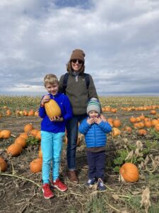 A mother and two boys standing and posing in a pumpkin patch
